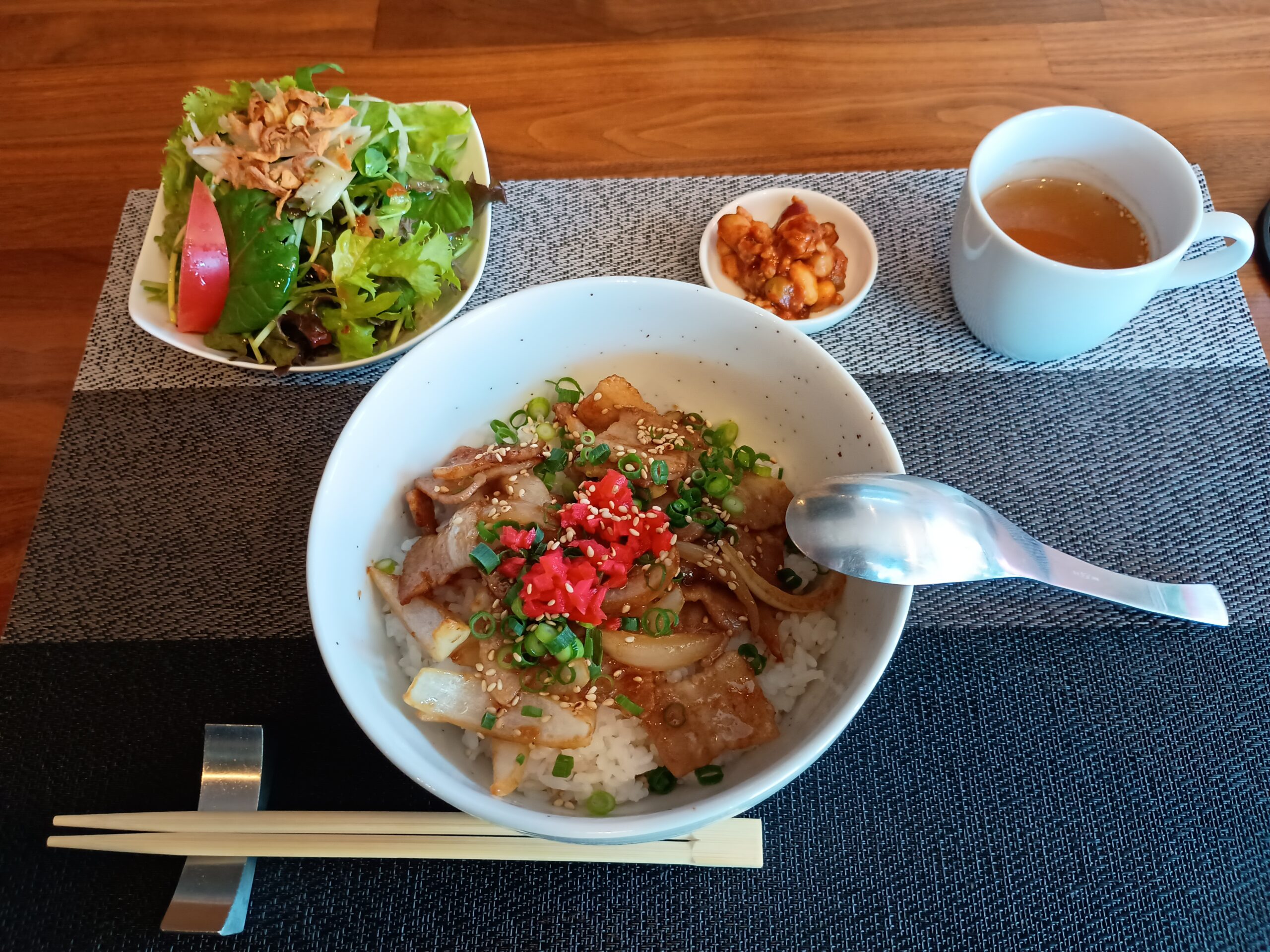白い丼に盛られたスタミナ丼。ニンニク醤油ダレの豚肉と玉ねぎの上に、紅生姜と刻み葱、白胡麻がのる。左手前にグリーンサラダ、奥中央にチリコンカンの小皿、右奥にスープカップ。箸と蓮華が添えられた、キッチン翔麗のランチセット。