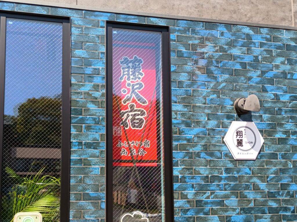 藍色のタイル張りの外壁に、「藤沢宿 ふじさわ宿商店会」の赤い縦長のぼり。右側の六角形の白い看板には「キッチン翔麗 SHORI ダイニングバー」の文字。