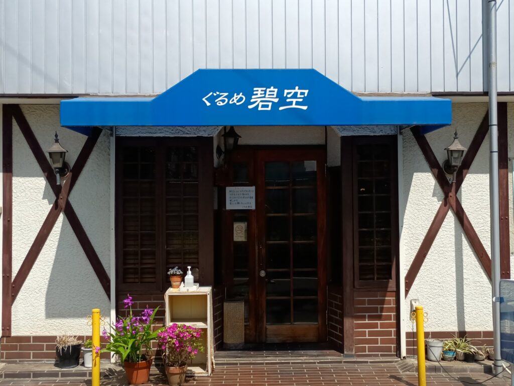 （外観）
 白い外壁に青い庇。「ぐるめ 碧空」の白文字。入口前に色とりどりの鉢植えが並ぶ、昭和の薫り漂う洋食レストランの正面。