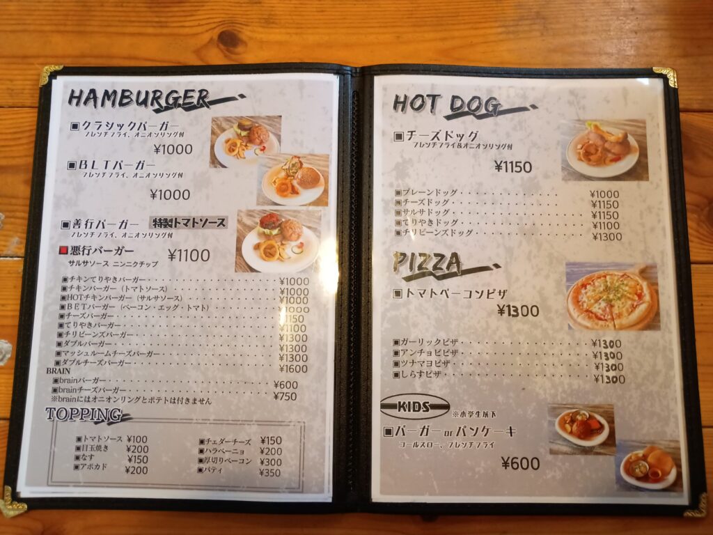 （メニュー：バーガー・ホットドッグ・ピザ）
メニュー表の見開き。左ページにクラシックバーガー¥1,000、善行バーガー¥1,100、悪行バーガーなど各種ハンバーガー。右ページにチーズドッグ、各種ピザ、キッズメニュー