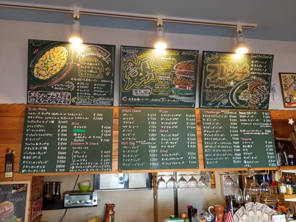 （店内壁メニュー）
店内カウンター上の壁一面に掲げられた黒板メニュー。マッケンチーズ、善行バーガー、フレンチトーストのイラスト付き看板と、サイドメニュー・価格一覧