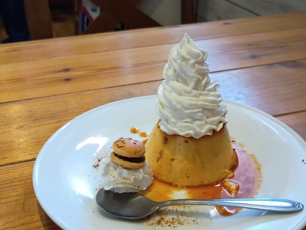（富士山盛りプリン）
富士山盛りカスタードプリン。プリンの上に富士山のように高く盛り上げたホイップクリーム、カラメルソースが流れ、脇にはミニマカロンが添えられている